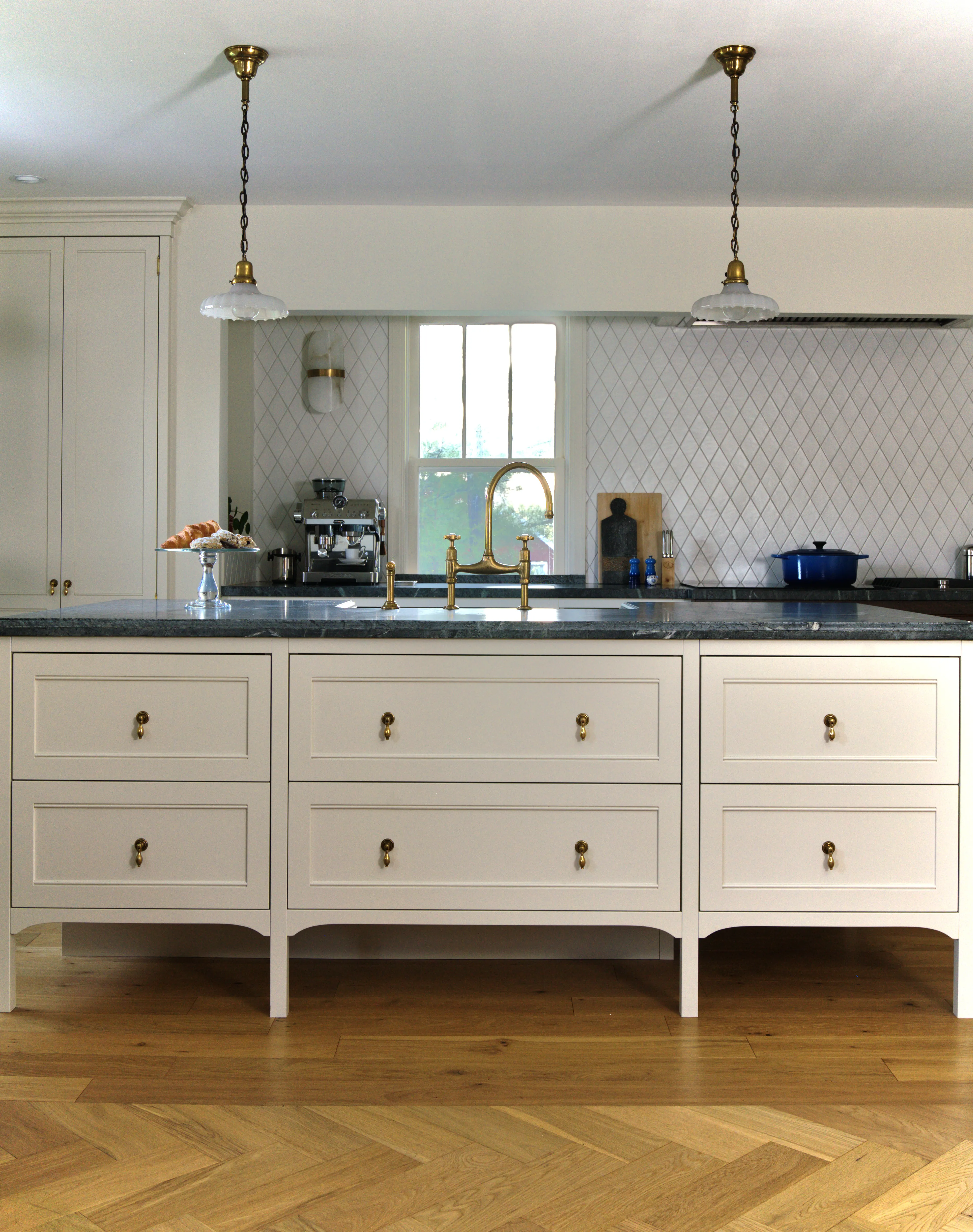 Custom English-style kitchen featuring a Fantasia soapstone island, deVOL bridge faucet in unlacquered brass, diamond-pattern tile backsplash, and white oak herringbone flooring, designed by Nathallie Isabel in a 1940s home in Aurora.