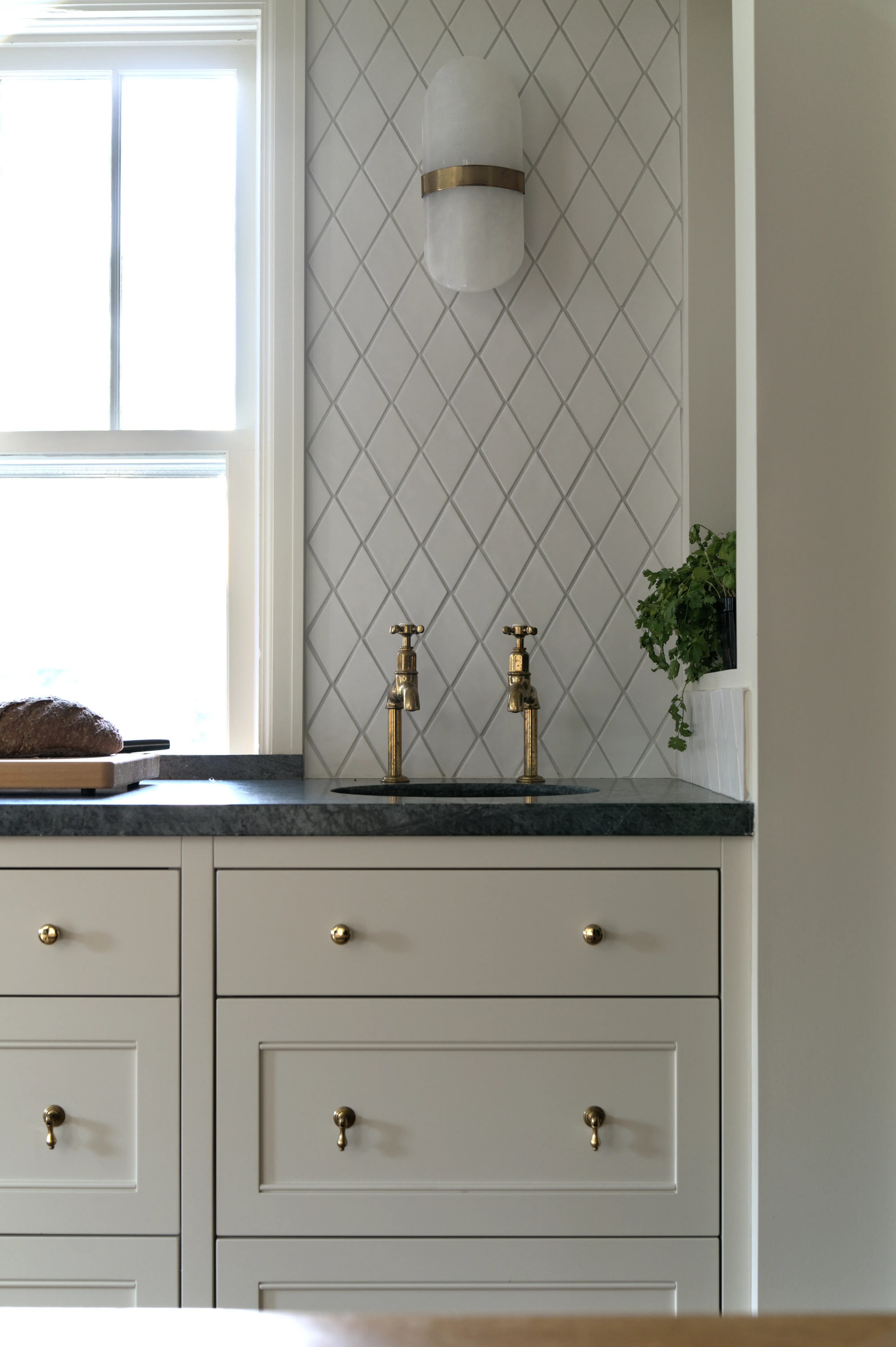 Secondary kitchen sink with deVOL Mayan taps in aged unlacquered brass, alabaster sconce, and diamond-pattern tile backsplash, in a custom bespoke kitchen designed by Nathallie Isabel.