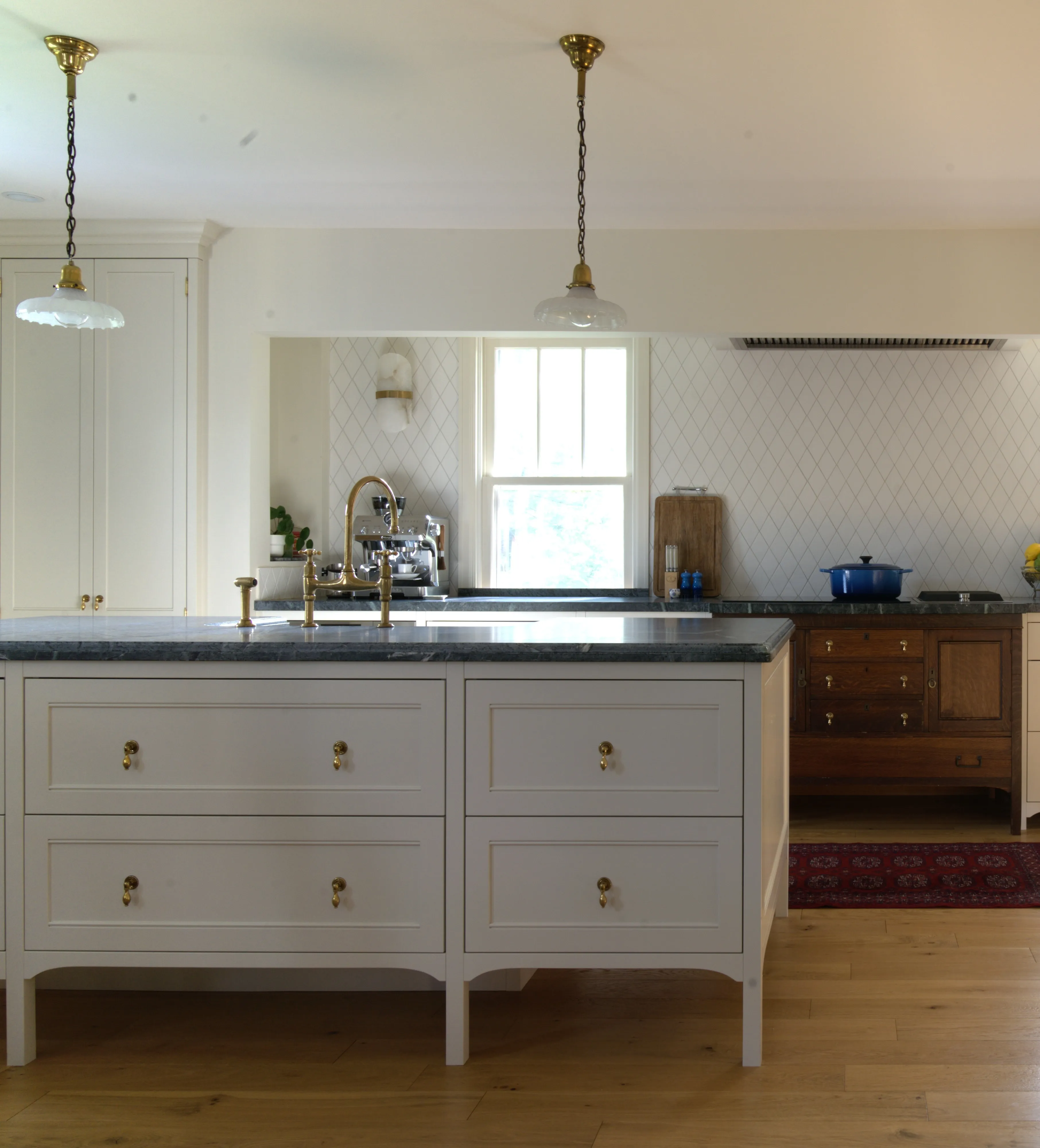 Modern English kitchen featuring a Fantasia soapstone island, custom cream-painted shaker cabinetry, integrated antique oak sideboard, and diamond-pattern tile backsplash, designed by Nathallie Isabel in a 1940s home in Aurora.